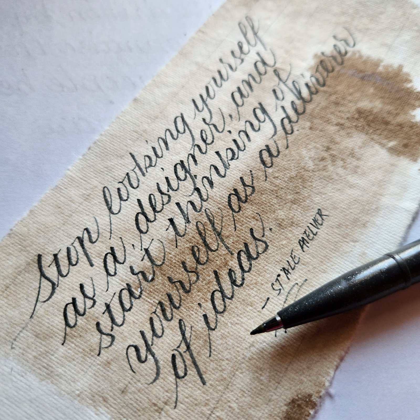 A quote written in brush pen on handmade paper with a coffee wash