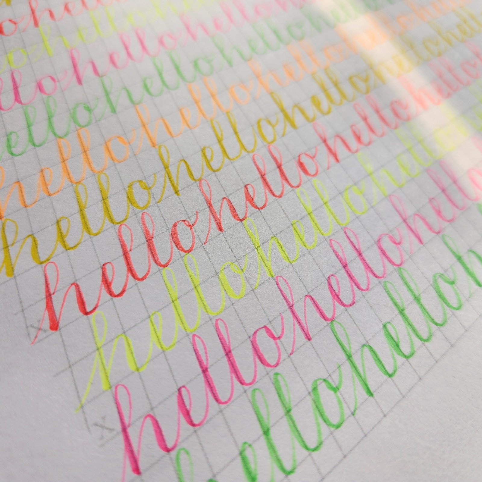 The word hello repeated in neon brush pen colours on grid paper