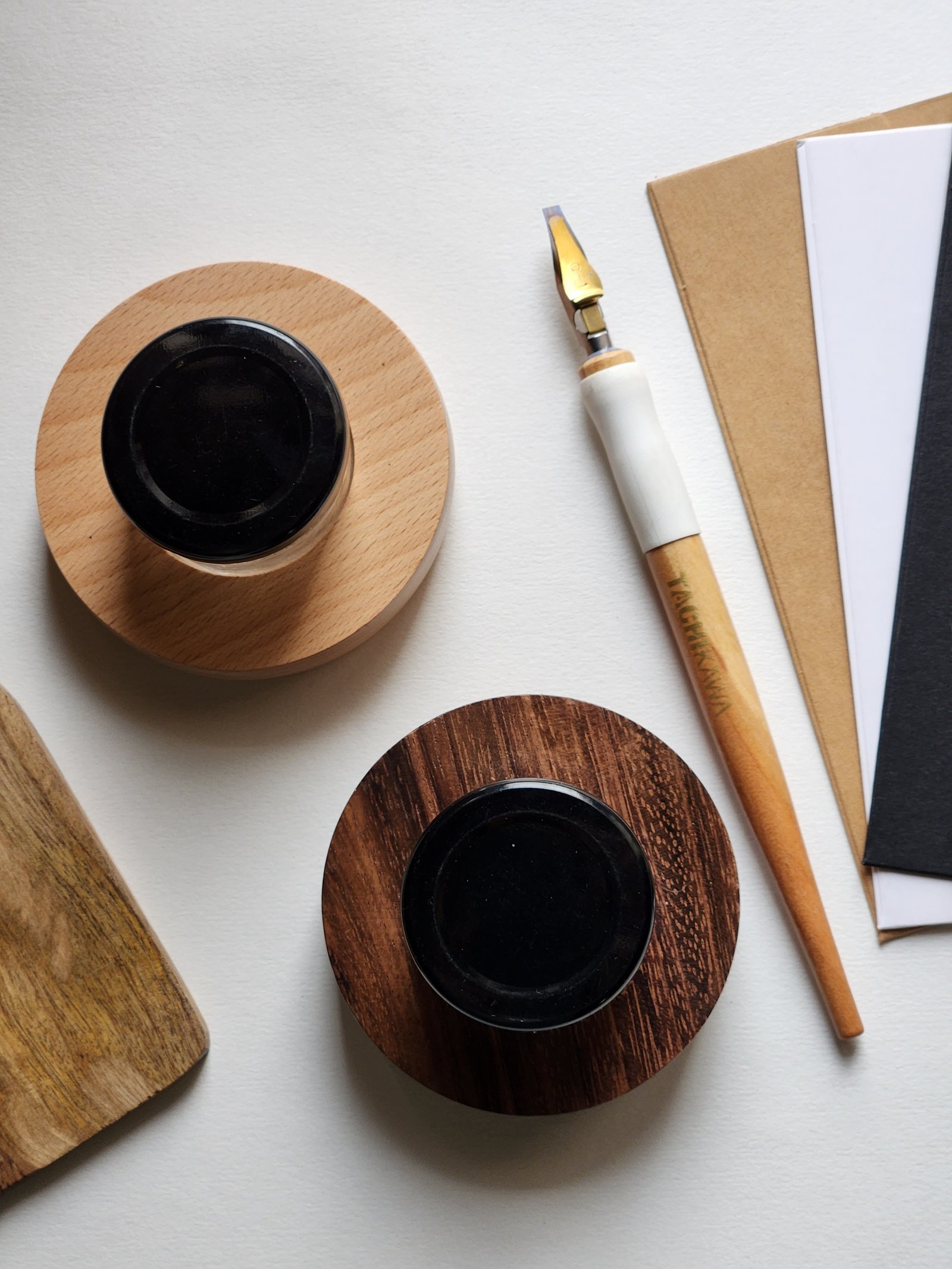 Two ink pots on wooden stands beside an oblique pen holder and folded papers